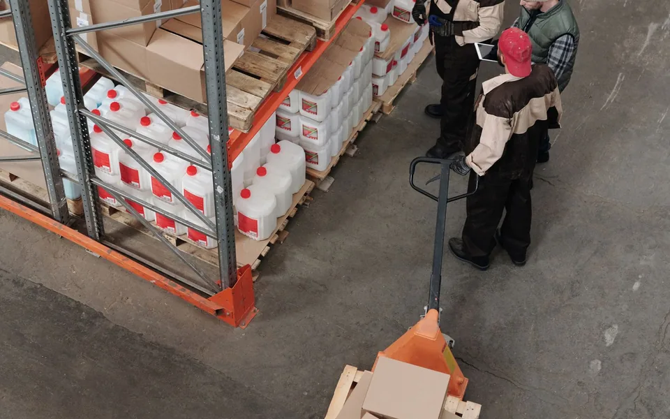 Warehouse team coordinating boxed goods beside pallet shelving
